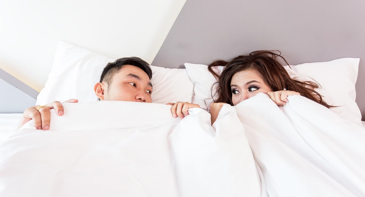 Paar sitzt sich im Bett gegenüber, beklemmende Stille und fahle Atmosphäre