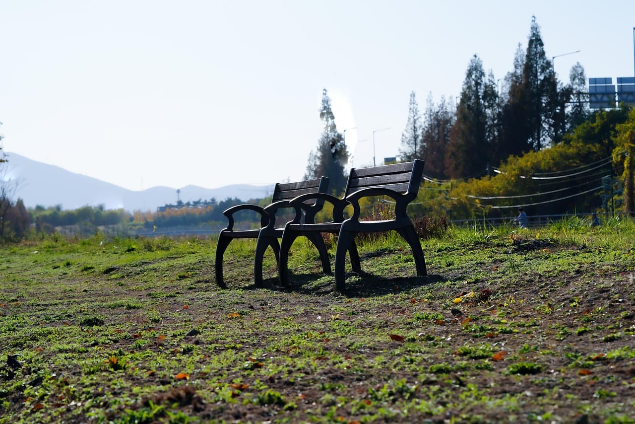 Zwei leere Parkbänke stehen nebeneinander auf einer Wiese vor einer Hügelkette