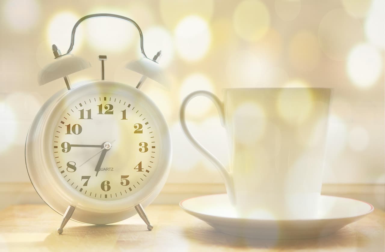 Weißer Wecker neben einer Tasse auf einem Holztisch im warmen Morgenlicht