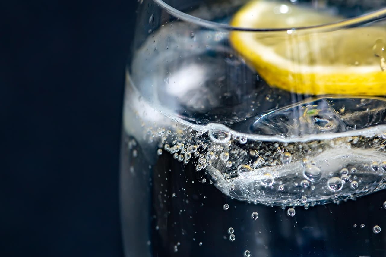Weiße Leinen-Bettwäsche im Morgenlicht, ein Glas mit Eiswürfeln und beschlagene Wassertropfen daneben