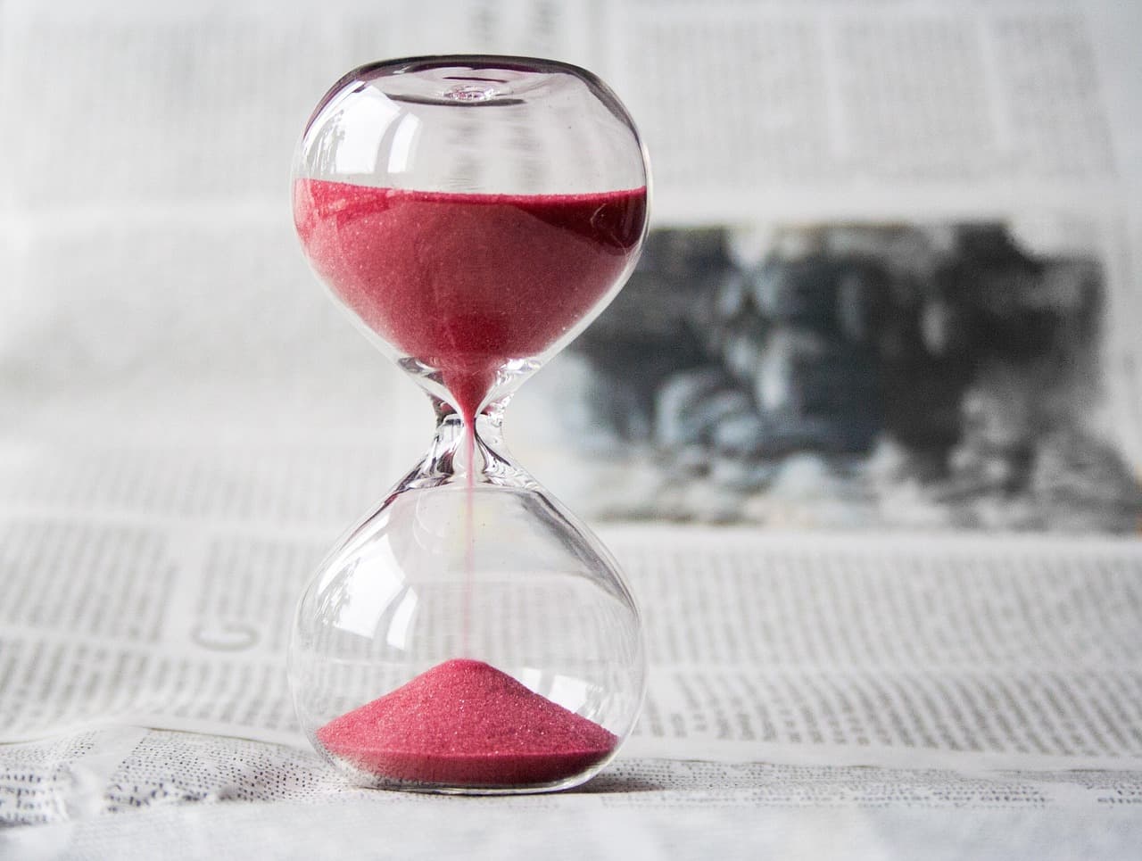 Sanduhr mit rosafarbenem Sand auf einer aufgeschlagenen Zeitung